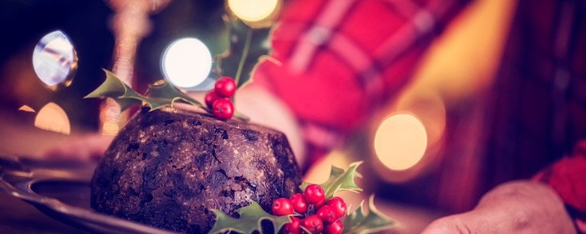 A Christmas pudding decorated with holly against a a back drop of soft lights